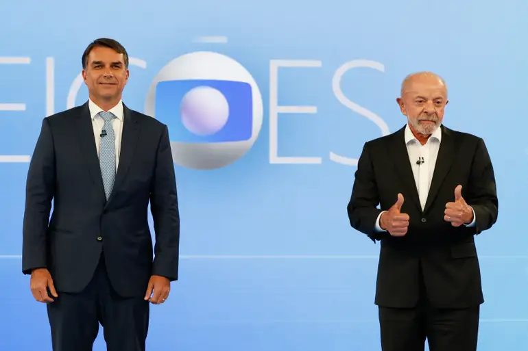 Lula e Flávio Bolsonaro durante debate presidencial; comparação mostra mudanças na votação em Cascavel e no Paraná entre os turnos.